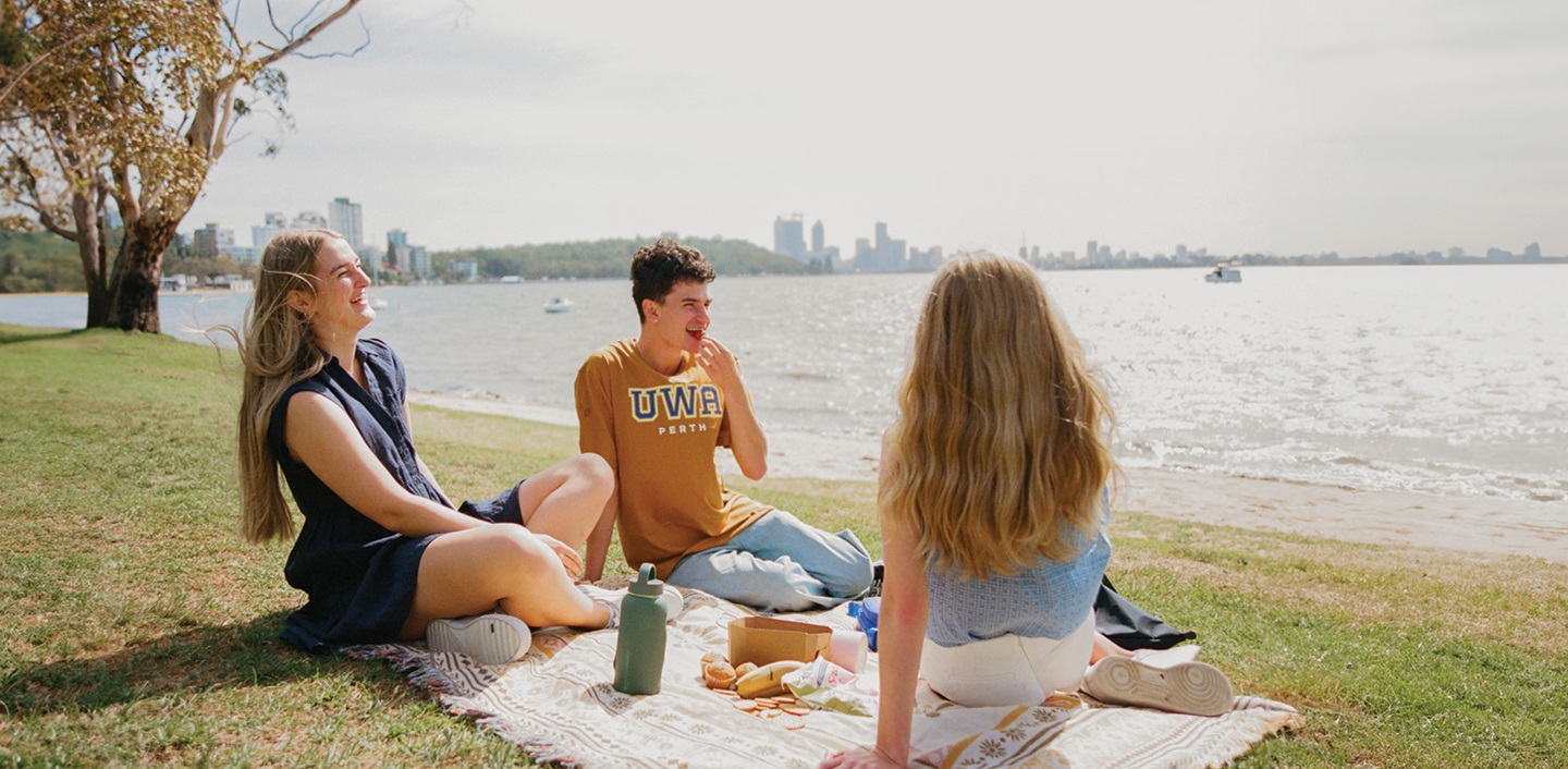 Three students sitting on the rive edge having a picnic
