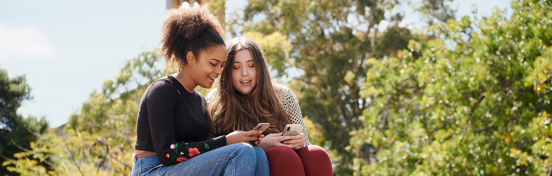 Two young women sitting on a wall looking at a mobile phone