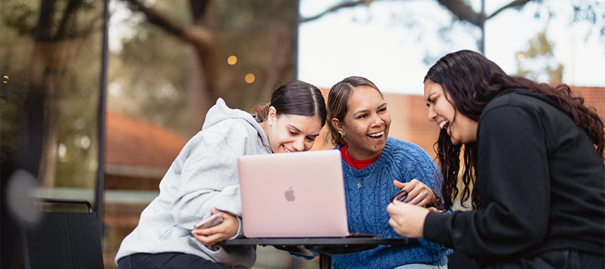3 indigenous students looking at a laptop and laughing
