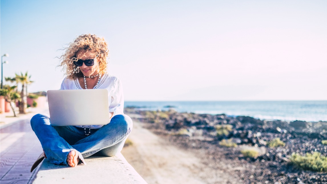 Woman sitting near beach and ocean using a laptop