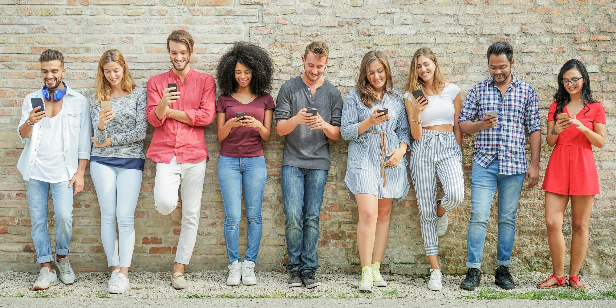 Group of young people leaning on a wall and looking at their mobile phones