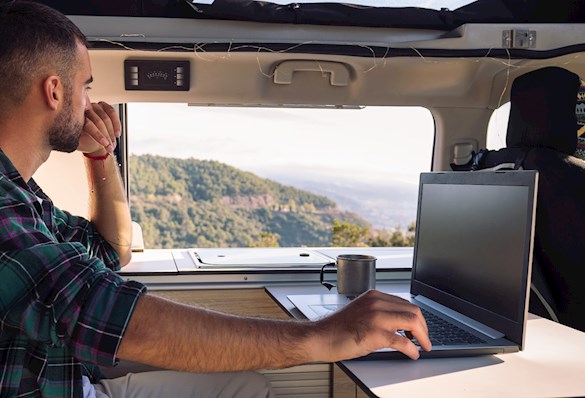Man working on his laptop from his camper van in the middle of the nature