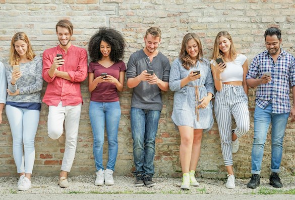 Group of young people leaning on a wall and looking at their mobile phones