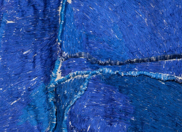 Detail of stitching in different blue threads covering the whole surface of several pieces of material stitched together with blue thread.