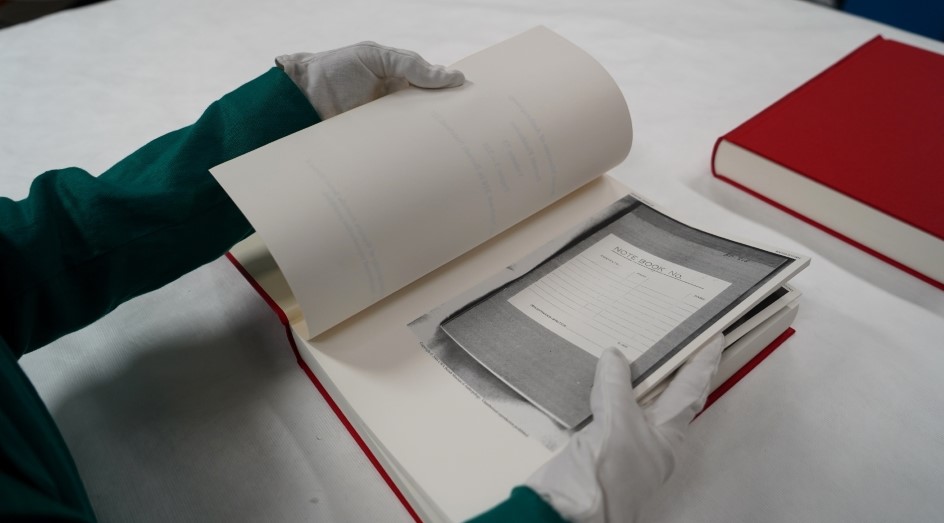 Hands opening a large bound book to a photocopied notebook page