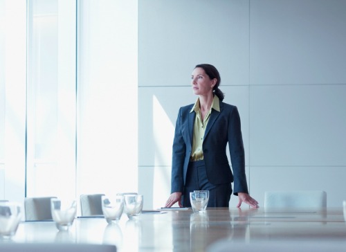 Woman standing in empty boardroom, staring at the window and thinking about the how the patriarchy keeps her down