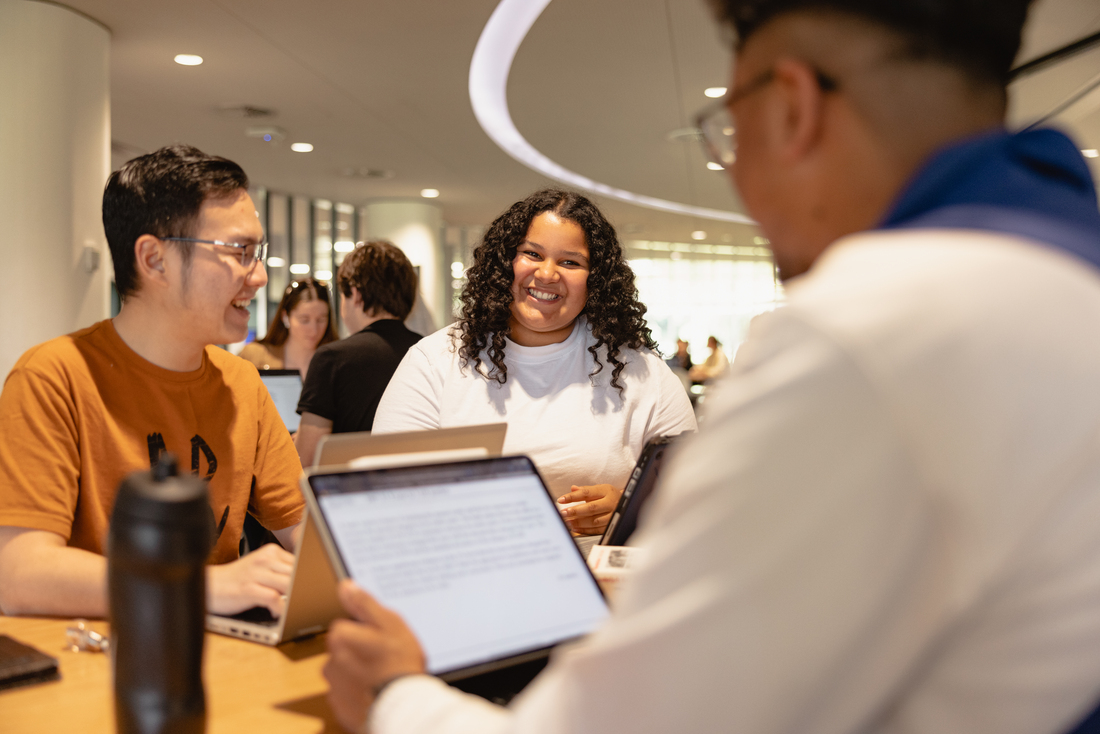 Students studying together in Reid Library, one student has their laptop screen in view and you can see they are reading a document. 