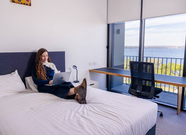 Image of a person sitting on a bed on their laptop