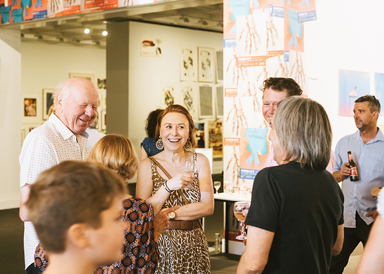A group of people of varying ages smile and laugh together in the gallery