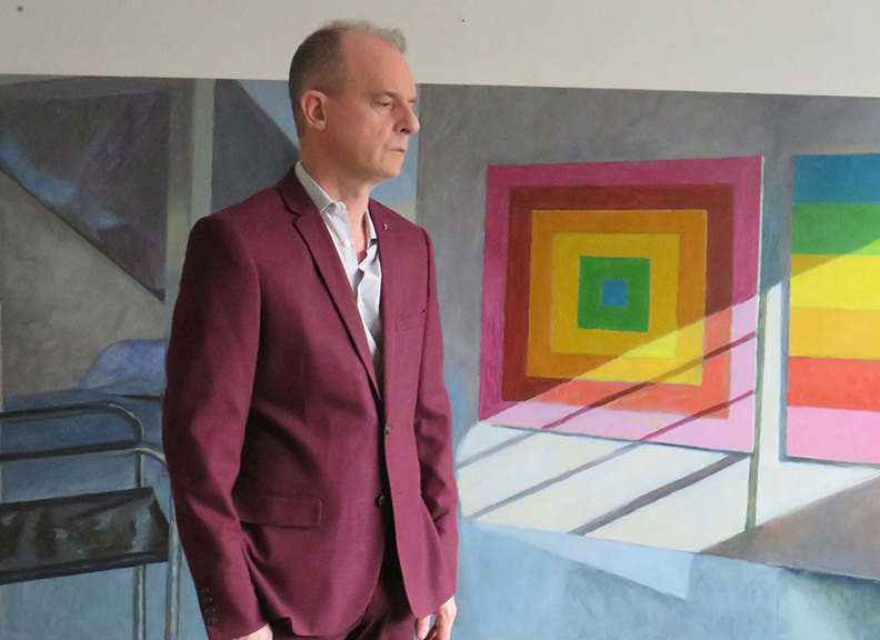 Kevin Robertson in purple suit standing in front of paintings