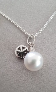 A large white pearl hangs from a silver necklace chain and photographed against a grey background