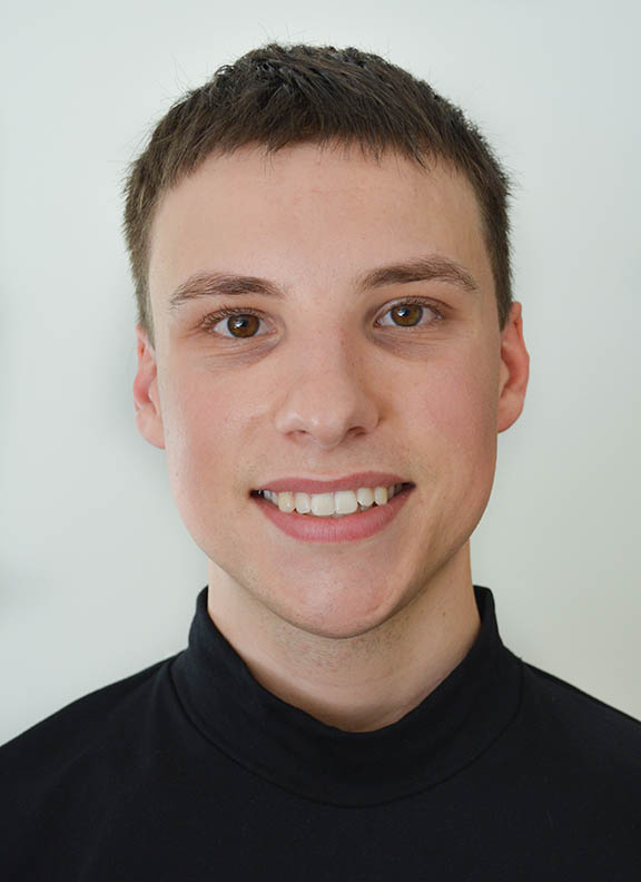 Photograph of a person with short brown hair wearing a black turtleneck shirt and smiling at the camera