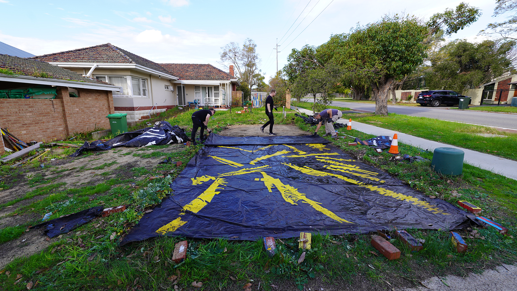 Photograph of a front lawn with a large black painting being unfolded by three people