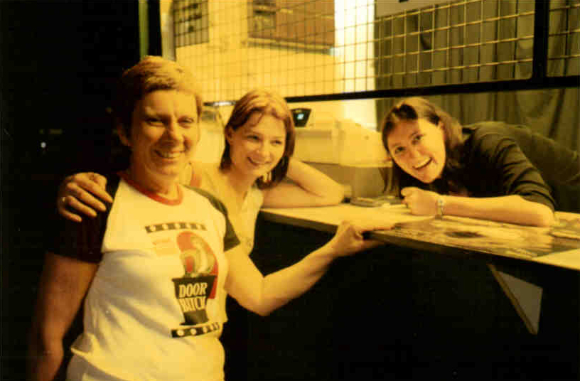 Aged yellow photograph of three women, one appears to be behind a ticket counter and another wears a shirt that reads 'door bitch'
