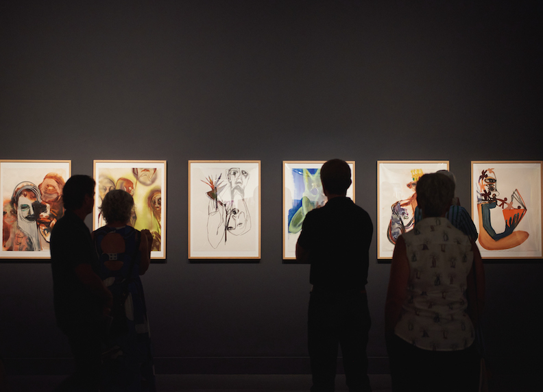 People looking at framed art in a darkened gallery
