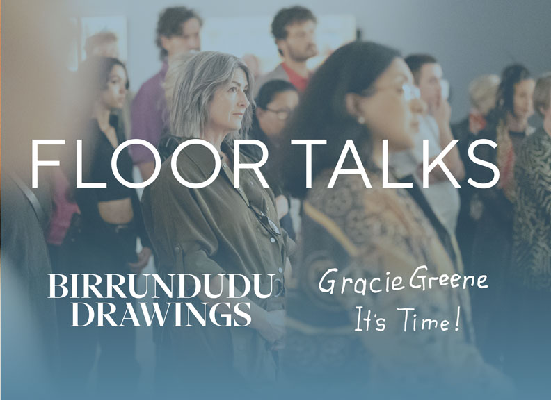 A group of people are standing and listening in an art gallery.