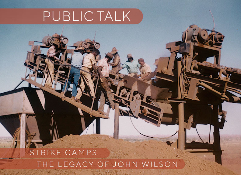 An old colour photo depicting a group of aboriginal men in work clothes and widebrim hats working together on a large piece of machinery in a desert landscape against a clear blue sky 