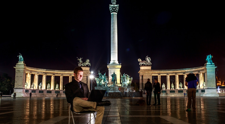 Adult businessman using laptop at monument at night