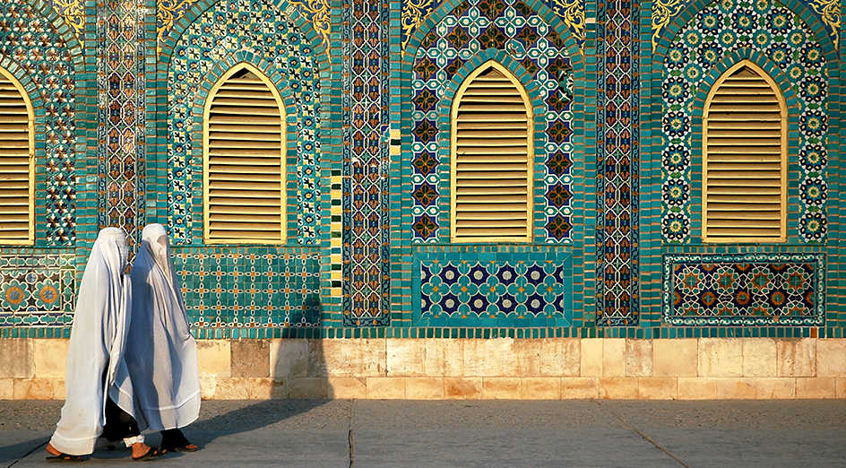 Two Afghanistan women walking past a mosaic wall