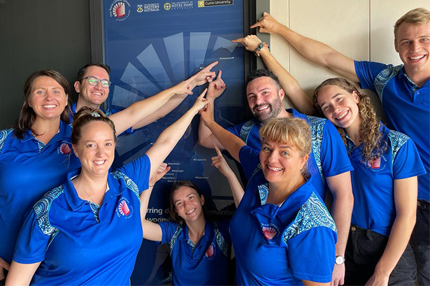 Group of Staff and Students pointing to a sign