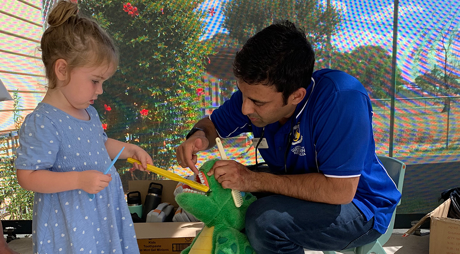 A UWA dental student with a young girl brushing the teeth of a soft toy