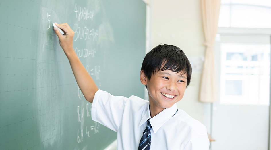 Young smiling Asian boy writing on blackboard