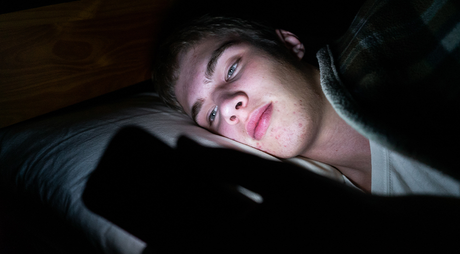 Teenage boy looking at his phone in bed