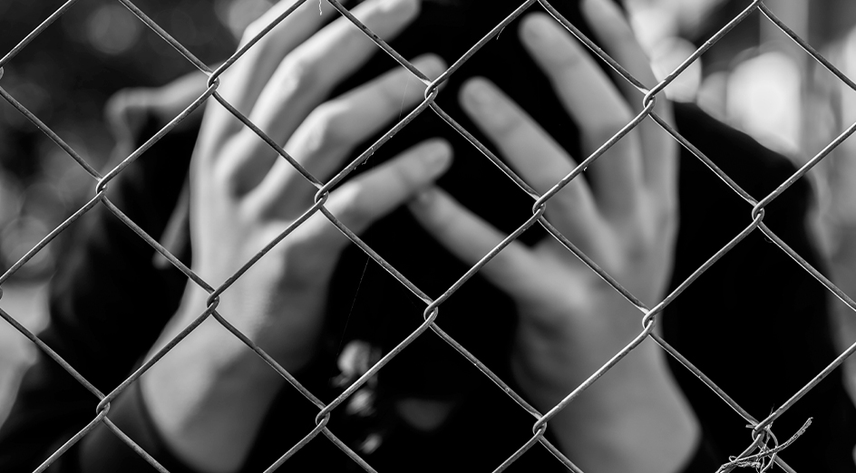 Youth with head in hands behind wire