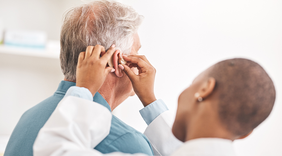 Audiologist checking elderly patients hearing aid