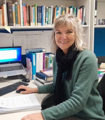 Madeleine Clews, Mid shot image of a woman sitting at a desk surrounded by a laptop and books