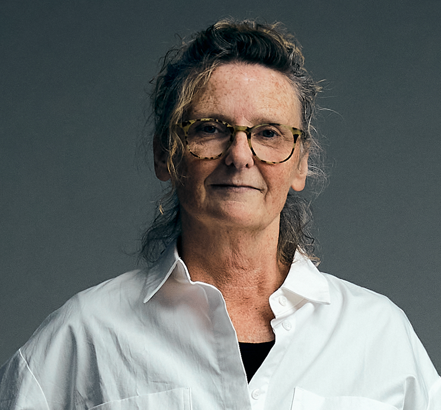 Portrait of a person wearing glasses and a white button-up shirt, photographed against a plain grey background.