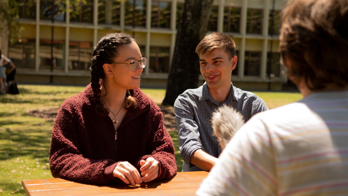 Three students sitting at a table outside talking