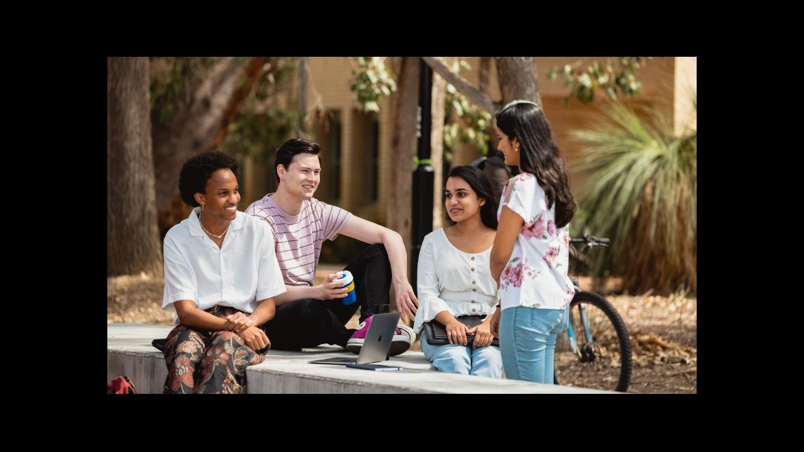 Three students sitting and one student standing and talking