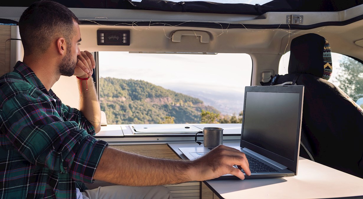 Man working on his laptop from his camper van in the middle of the nature