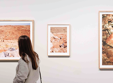 Visitor viewing framed landscape artworks in a contemporary gallery exhibition.