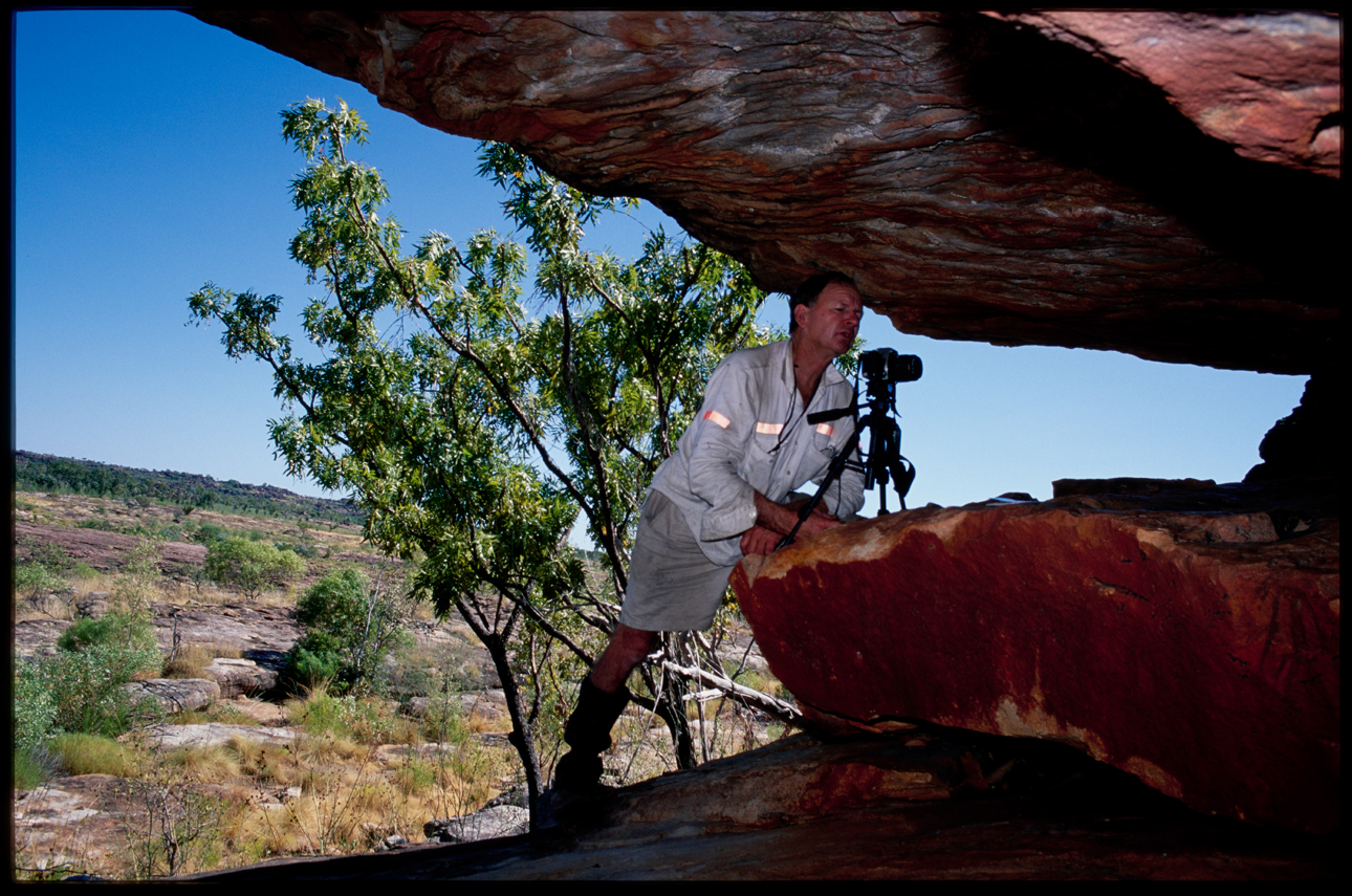 photographer with SLR camera standing within a rock formation taking photo of rock art