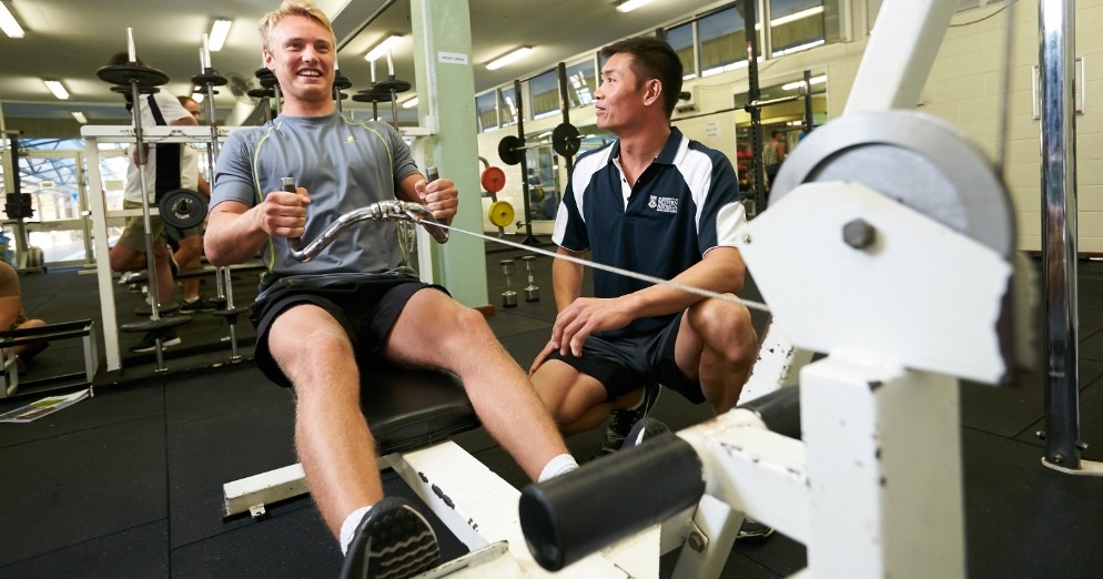 Male working at a gym machine and being assessed by a staff member