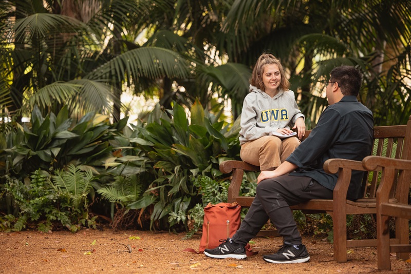 Two students sitting on a bench in the Tropical Grove