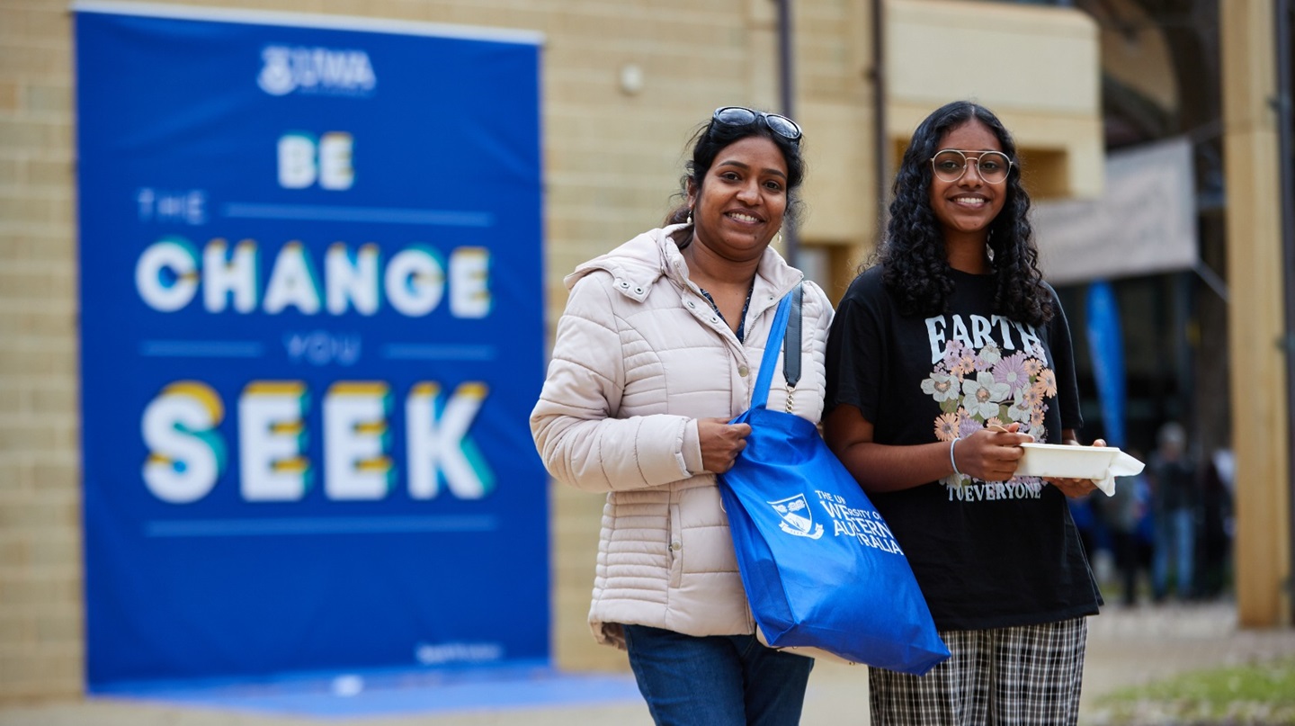 Parent and teenager at UWA Open Day standing in front of sign that says be the change you seek