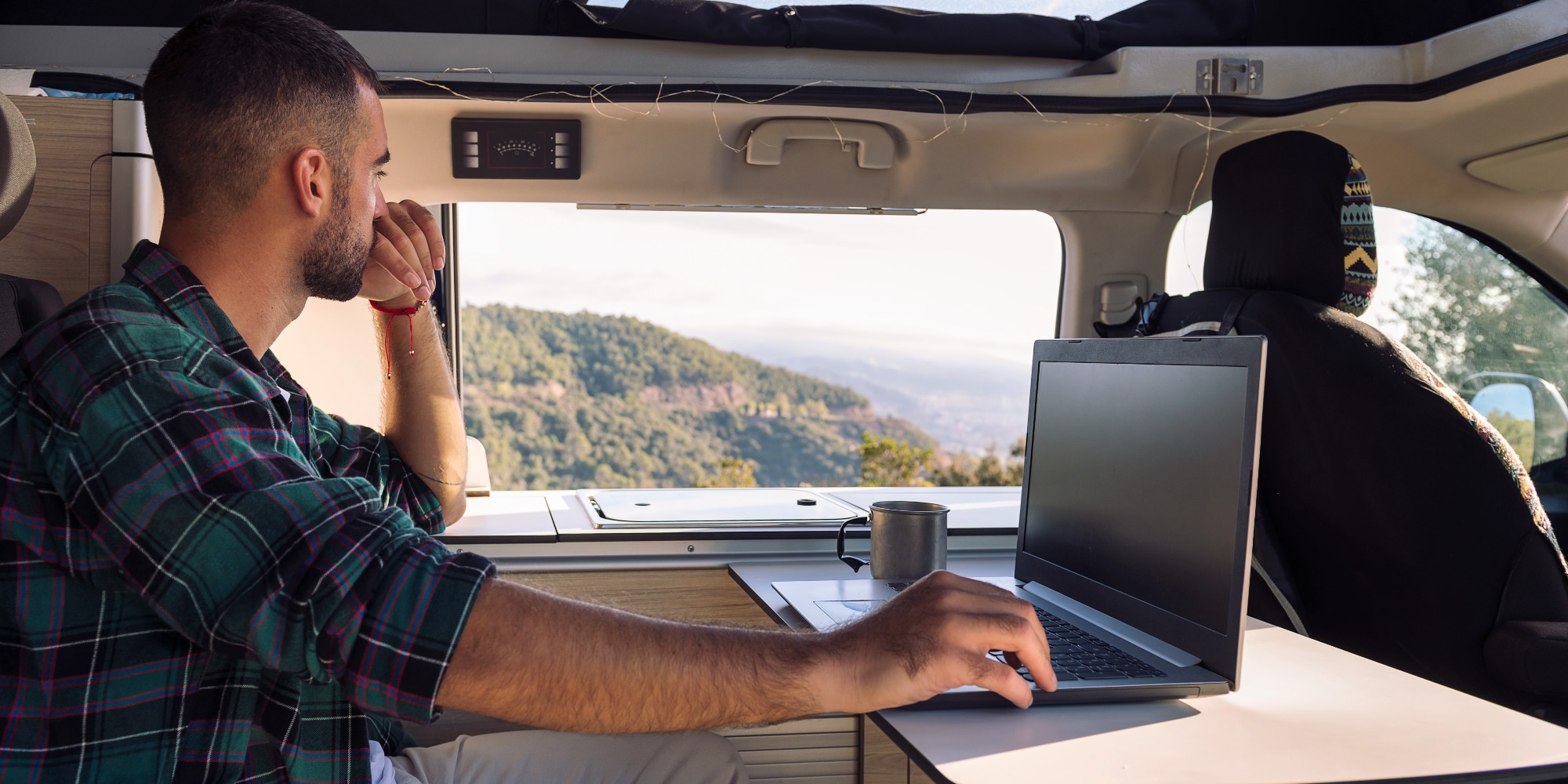 Man working on his laptop from his camper van in the middle of the nature