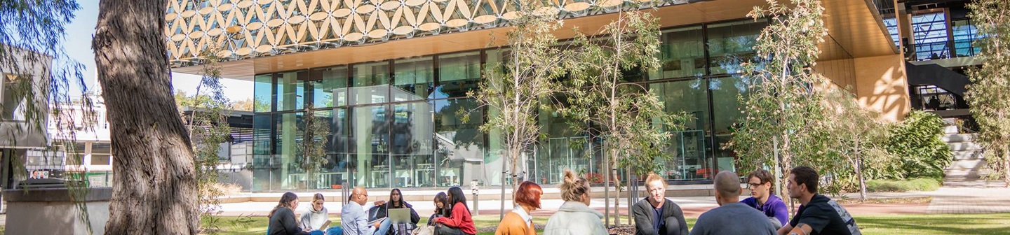 Large group of male and female students sitting down on the grass outside of EZONE building