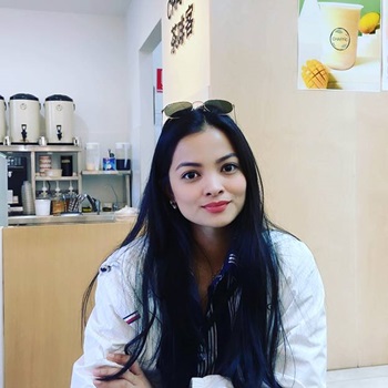 Female sitting down in cafe, smiling with dark hair and sunglasses on top of her head
