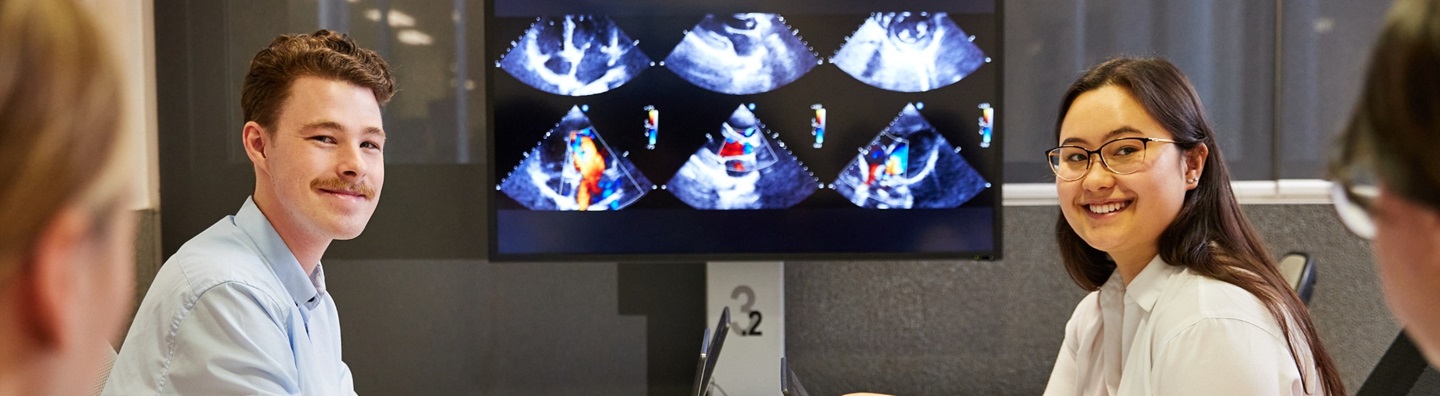 Medical students smiling sat with laptop with medical imagery in background