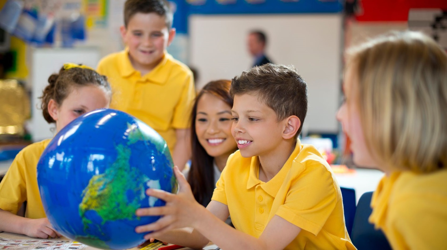 School students in a classroom studying a globe. 