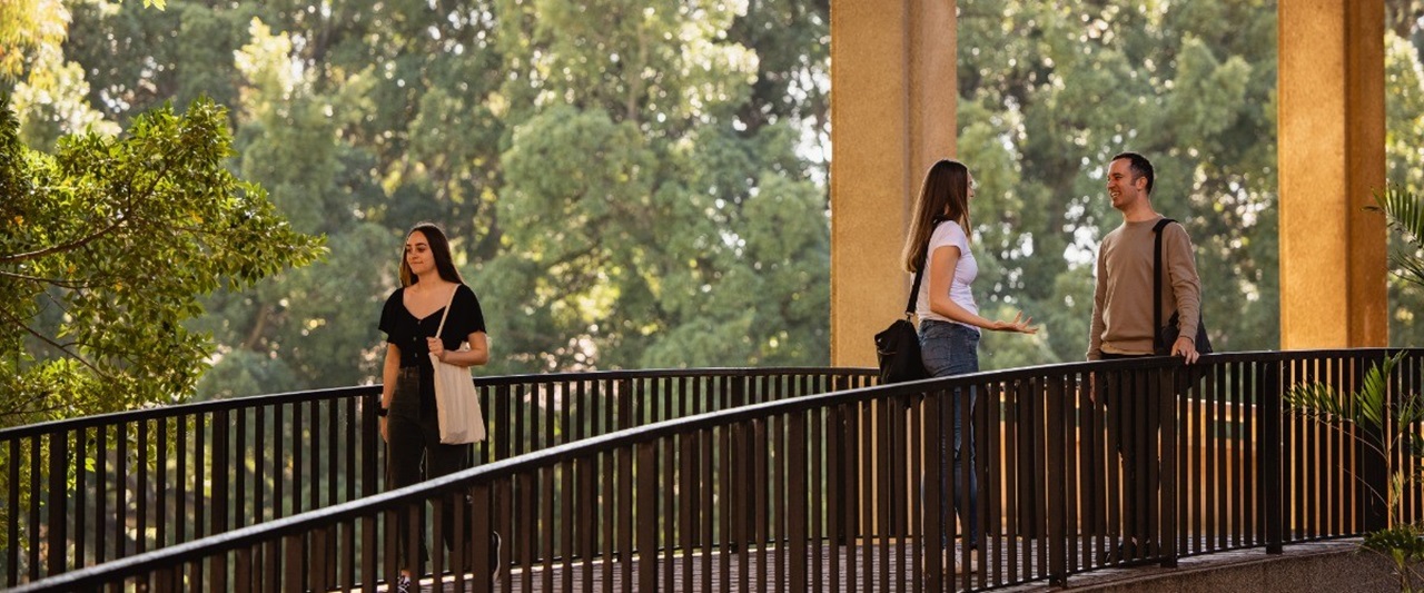 Students talking on Reid Library bridge, student walking past