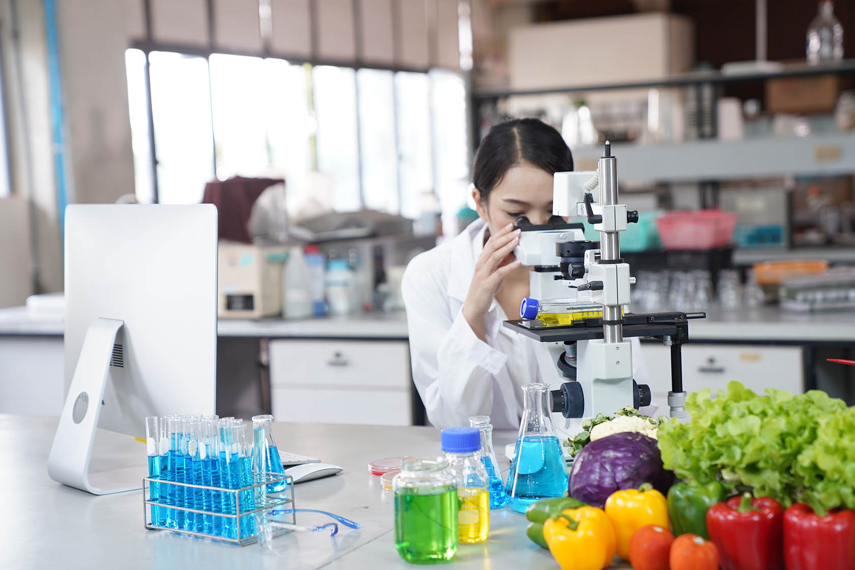 Female looks through microscope with food and test samples nearby