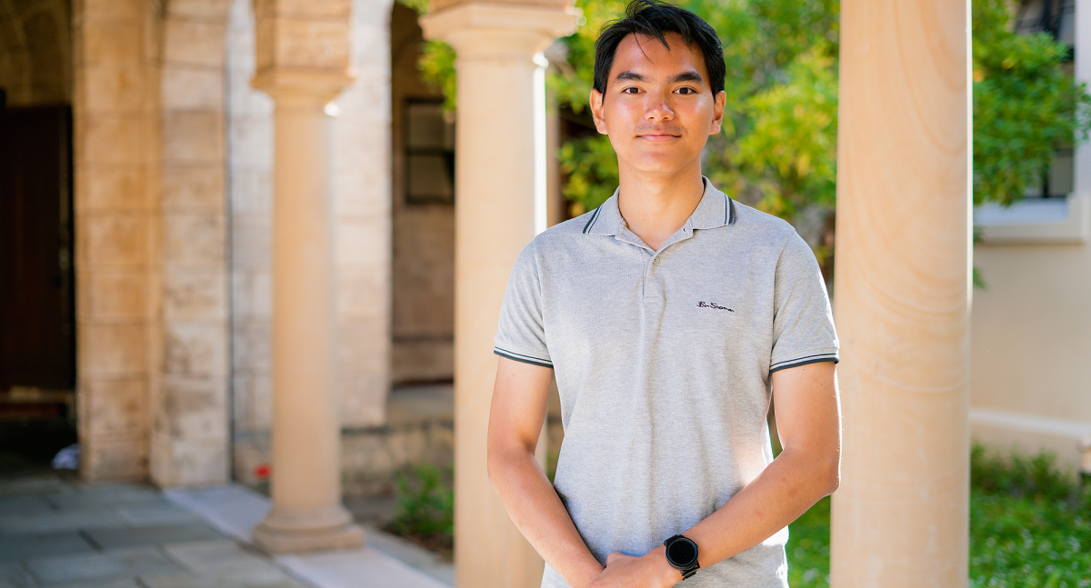 Juan smiling standing under arches with arms down holding hands at his front