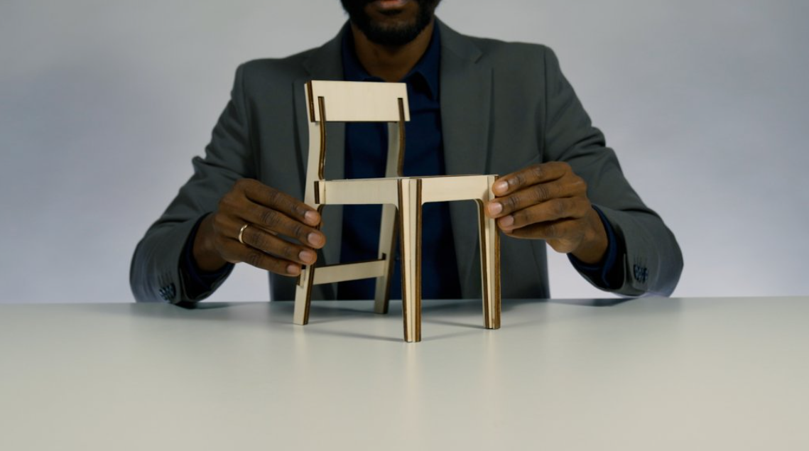 Mid-shot image of a person whose face is out of frame touching a small golden chair that is placed on top of a table. 