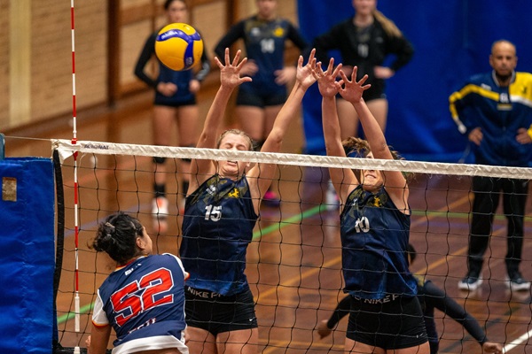 Two UWA Volleyball Club members jump to block a spike by an opposing team member