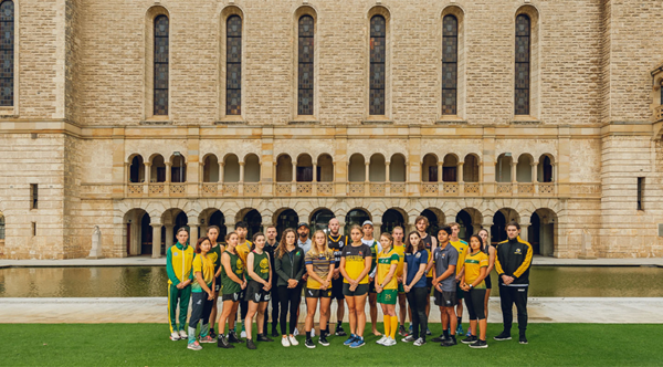 A group of elite student athletes, dressed in green and gold Australian representative uniforms, stand in front of Winthrop Hall